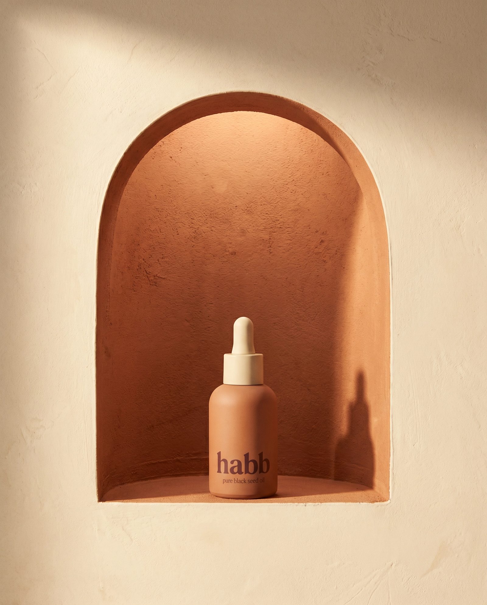 habb terracotta bottle in a saturated terracotta arch niche on cream plaster, warm morning light